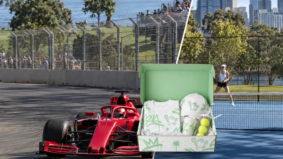 Formula 1 car on a Melbourne park circuit beside a tennis court, with an open custom printed mailer box of event merchandise in the foreground